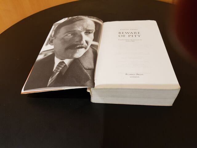Een opengeslagen boek op een zwarte tafel. Links staat een afbeelding van auteur Stefan Zweig, rechts de titel 'Beware of Pity'.