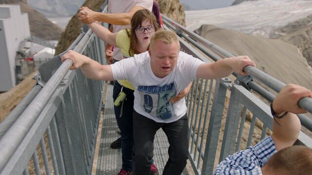 twee deelnemers aan Down the road klimmen hijgend een stijle metalen trap op die zich op grote hoogte bevindt