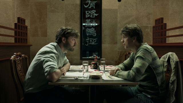 Twee mannen zitten tegen elkaar aan een tafeltje in een Chinees restaurant. Ze kijken elkaar indringend aan.