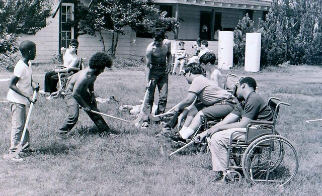 Zwart-wit afbeelding. Een groep jongeren speelt hockey. Sommigen zitten in een rolstoel.