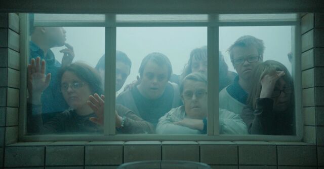 A group of people is peeping in through a window. They look worried.