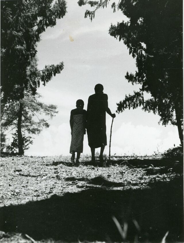 Zwart-wit afbeelding van Katutu. Hij wordt afgebeeld met een stok en wordt begeleid door een jongen