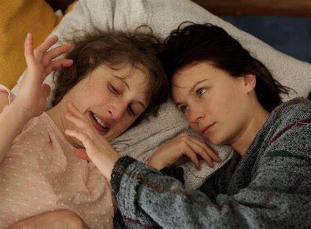 Elisa en haar zus Manon liggen samen in bed. Elisa kijkt naar Manon; hun handen raken elkaar net niet.