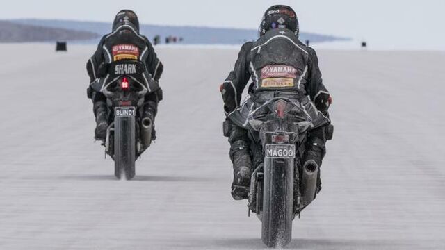 Twee motorrijders in zwarte pakken rijden weg van de camera, de Australische woestijn in.