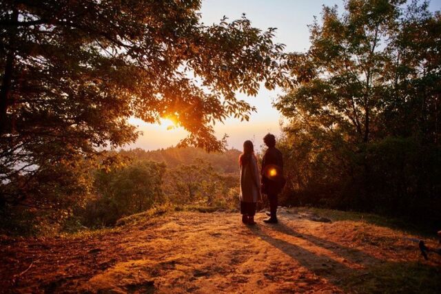 Still uit de film Radiance. Een man en een vrouw kijken vanuit een bebosde omgeving uit naar de zonsopgang.
