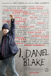 Een man in jeans steekt voor een muur waar met zwarte verf de tekst "I, Daniel Blake" werd opgeschilderd krijgshaftig zijn linkervuist in de lucht.